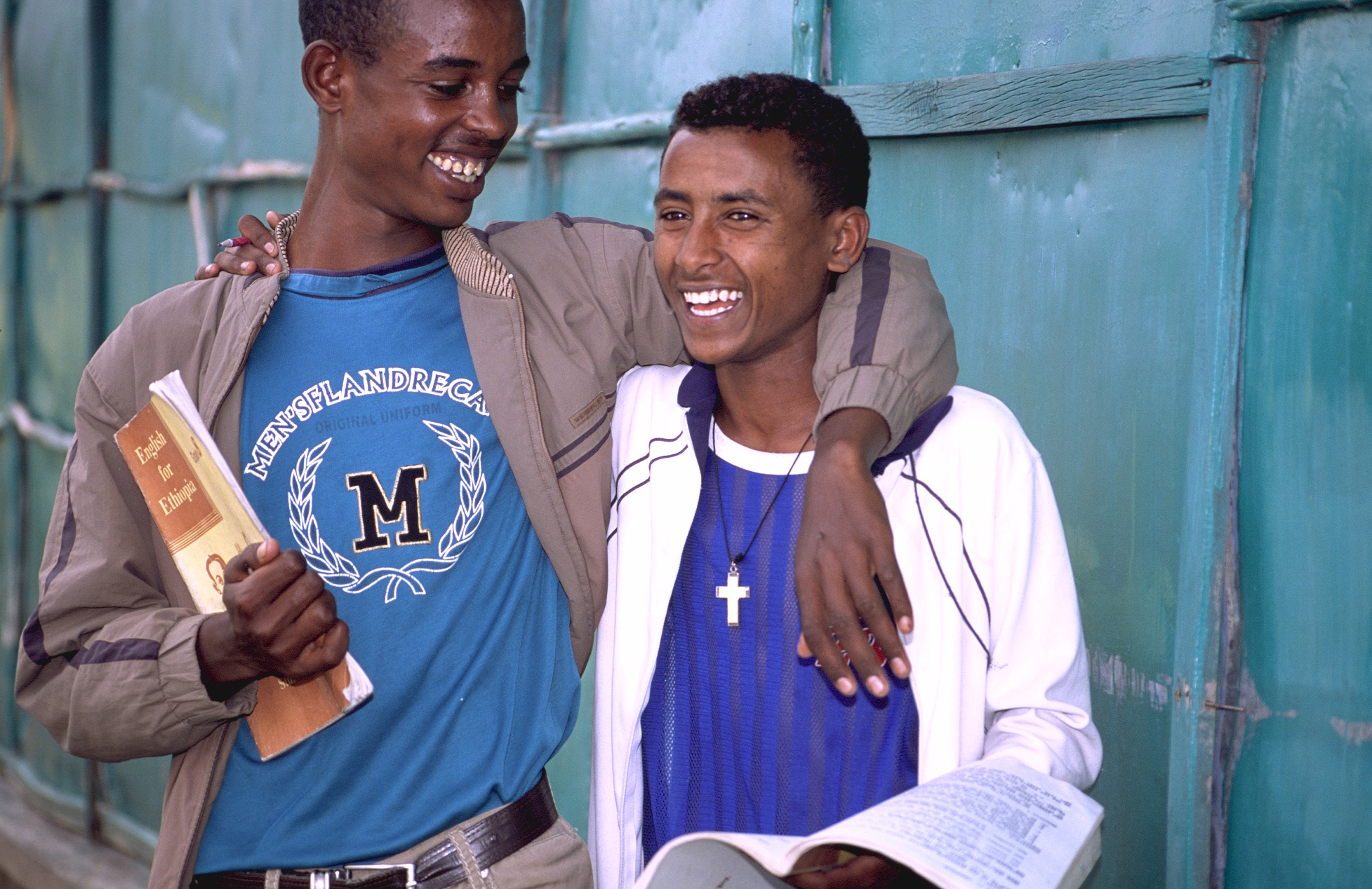 Two happy looking(cheeful) boys, with one holding the book and his arm around the other