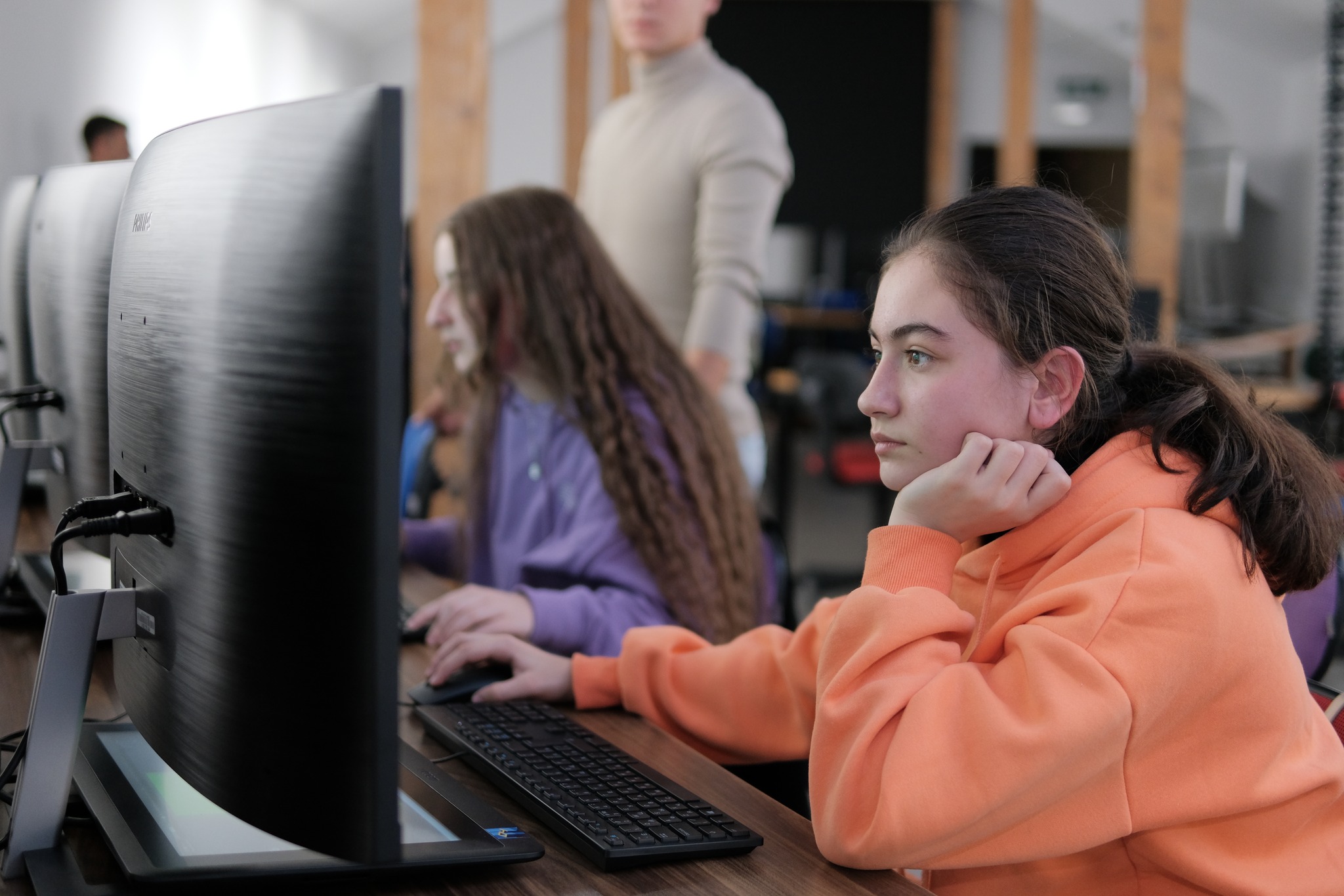 Girl in orange hoodie sitting in front of a computer