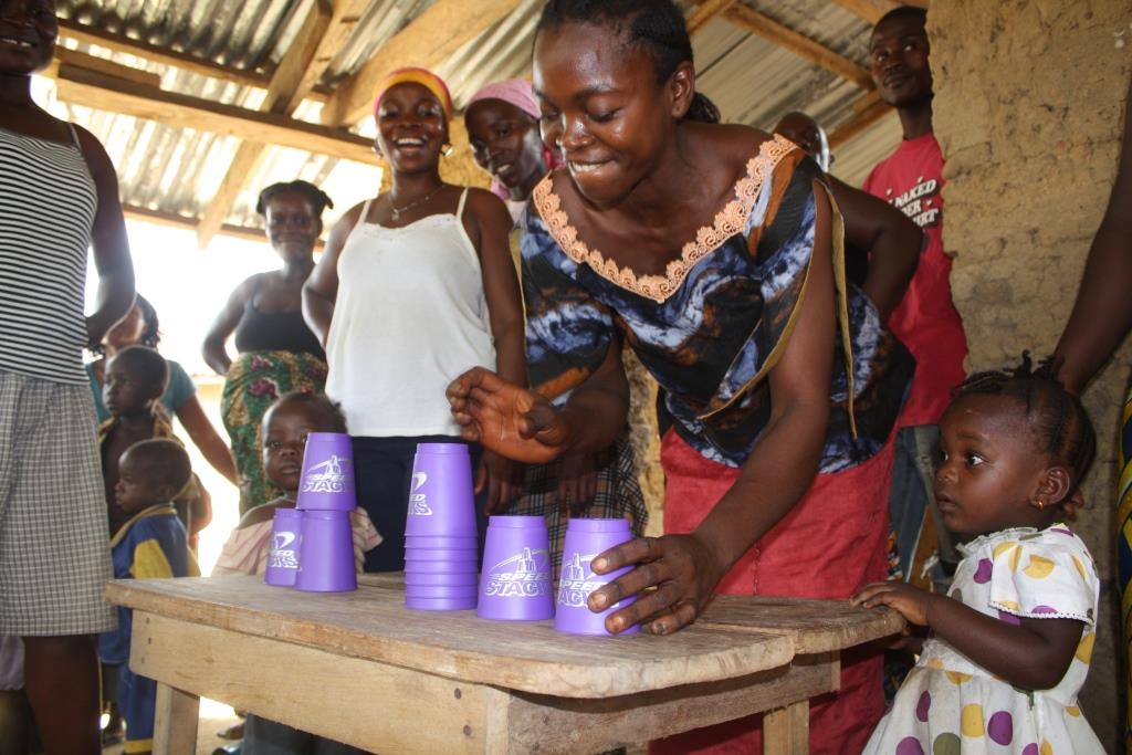 A woman is playing with the cups on the table while other smiling women are watching her doing it. Photo by Making Cents