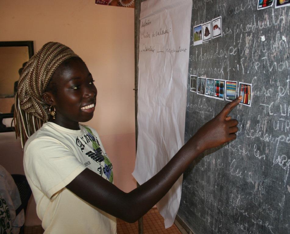 A smiling girl is pointing towards a picture on the blackboard, Photo by Making Cents