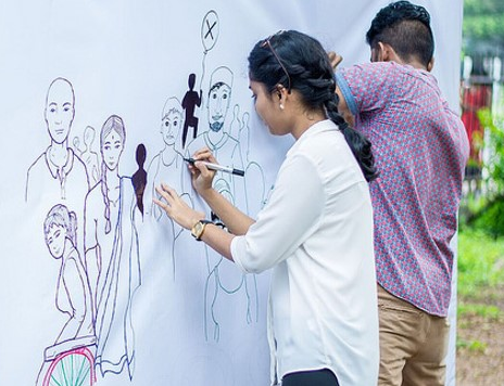 A young man and a woman are drawing illustrations on a white wall. 